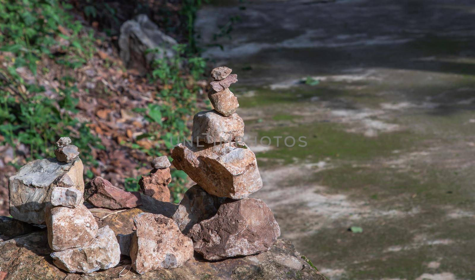 Balanced stone tower on walkway up the mountain with green plants in the background. No focus, specifically.