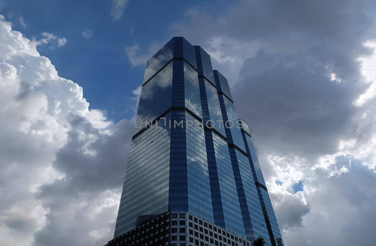 Bangkok, Thailand - July 10, 2019 :  Angular geometric mirror cladding on a modern building with repeating structure and reflected sky and clouds. No focus, specifically.