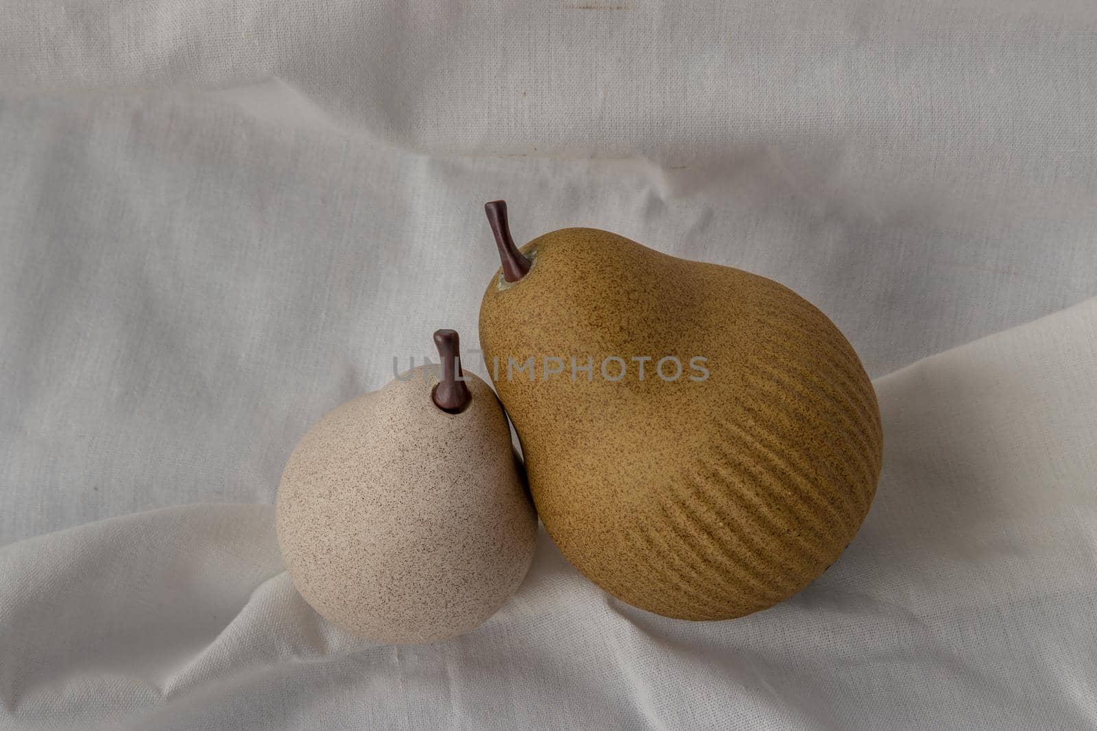 Two ceramics pear fruits on white fabric background. Ceramic tableware, Home decor, Copy space.