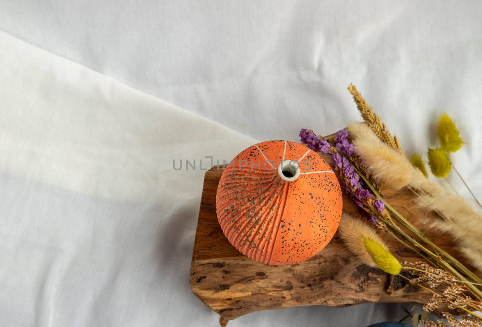 Beautiful small orange ceramic vase and Dried flowers on wooden logs with White fabric background. Ceramic tableware, Home decor. Top view, Copy Space.