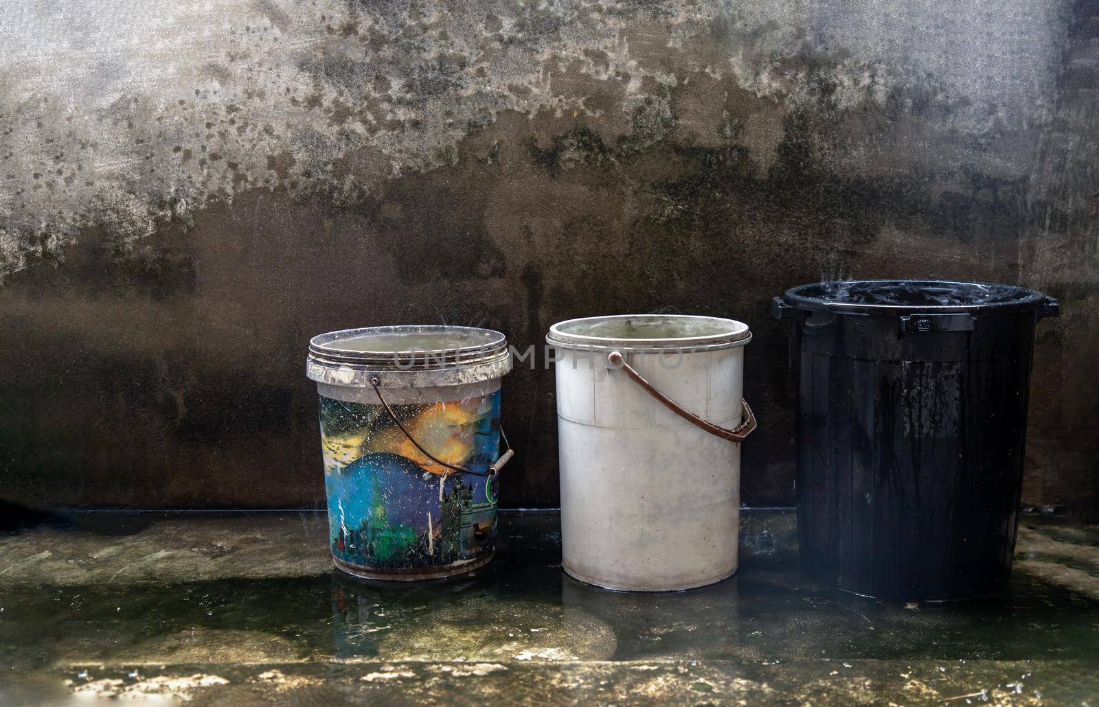 Blue, White and Black Old Plastic Buckets Filled with Rainwater on the cement floor on a rainy day. While it rains, we can take the container over the rainwater to keep it. Save water, save environment concept, Copy space, No focus, specifically.