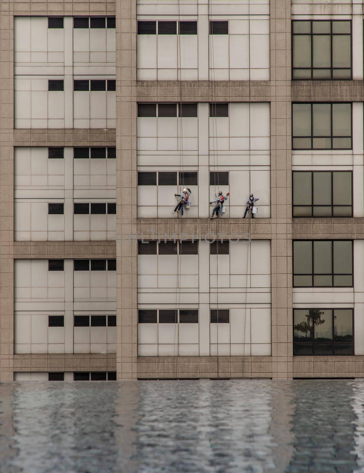 Group of workers cleaning windows service on high rise office building with reflection from swimming pool. Selective focus.