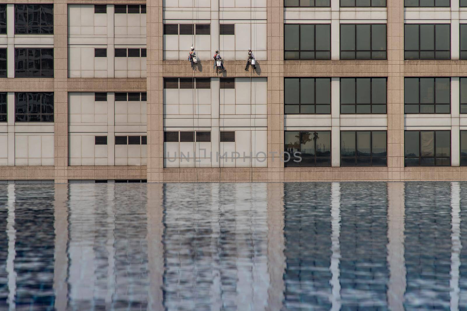 Group of workers cleaning windows service on high rise office building with reflection from swimming pool. Selective focus.