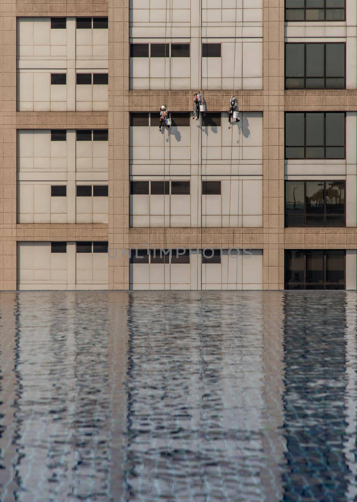 Group of workers cleaning windows service on high rise office building with reflection from swimming pool. Selective focus.