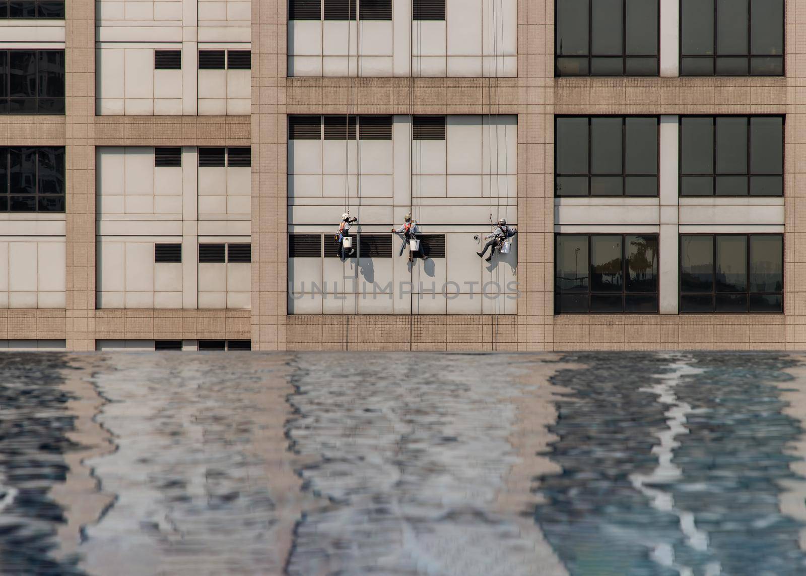 Group of workers cleaning windows service on high rise office building with reflection from swimming pool. Selective focus.