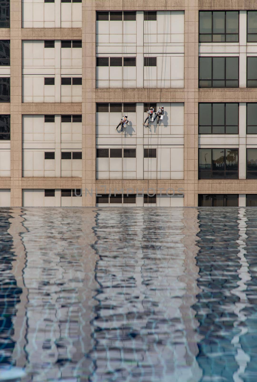 Group of workers cleaning windows service on high rise office building with reflection from swimming pool. Selective focus.