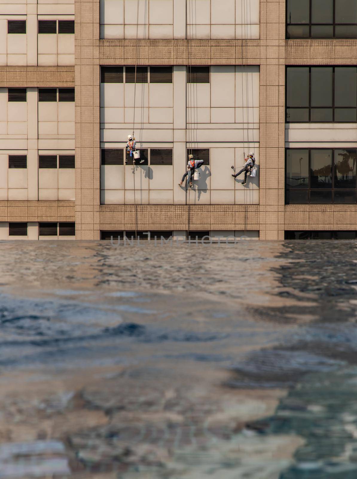 Group of workers cleaning windows service on high rise office building with reflection from swimming pool. Selective focus.