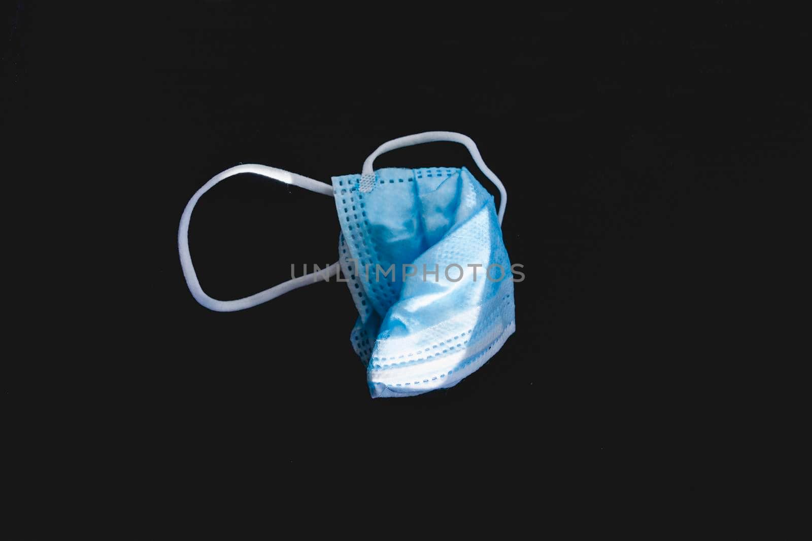 Disposed plastic protective face mask, on a dark background. by alvarobueno