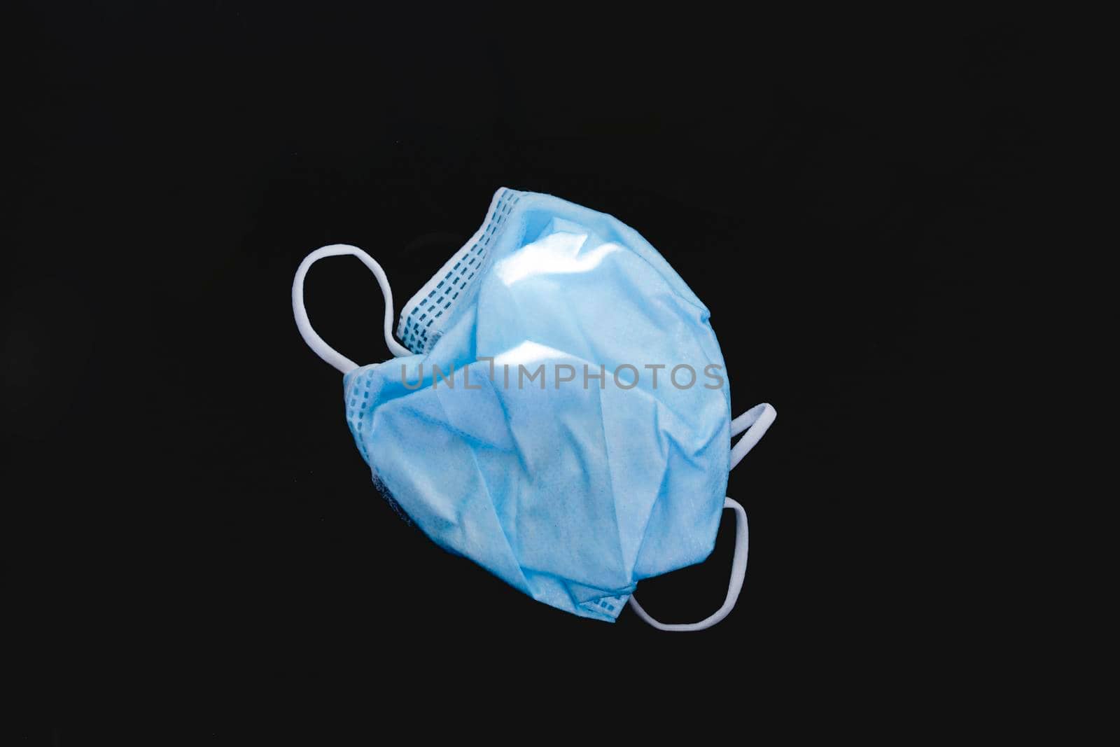 Disposed plastic protective face mask, on a dark background. by alvarobueno