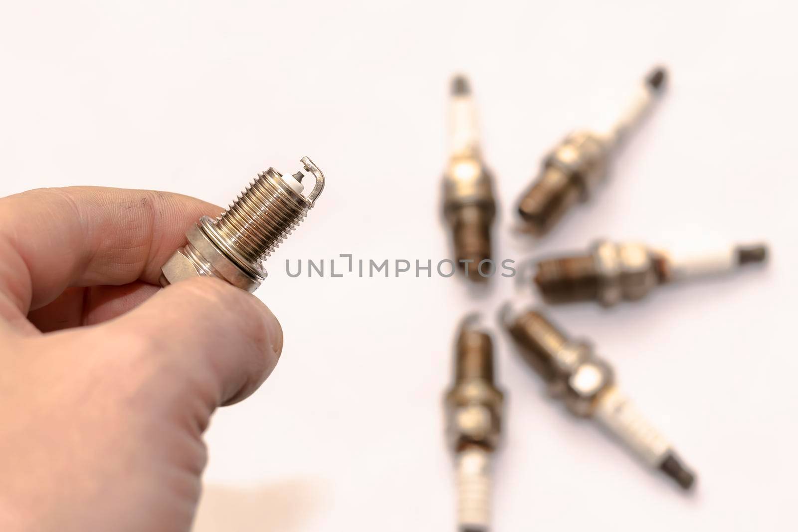 a man's hand holds a gasoline car spark plug against a background of worn-out old used-up, resource parts on an empty clean white background