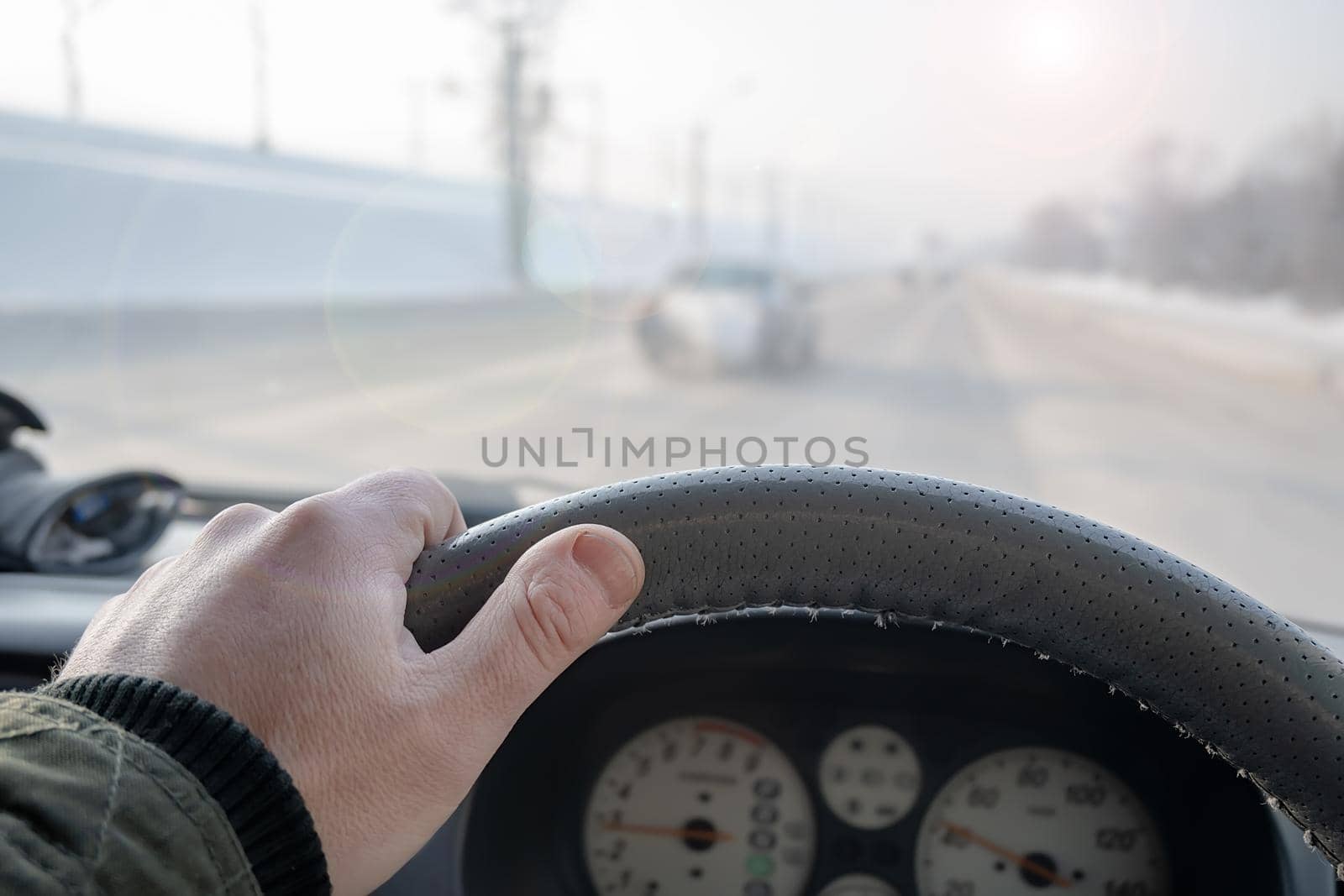 the hand of a man on the steering wheel of a car that is driving on a snow covered slippery icy winter road