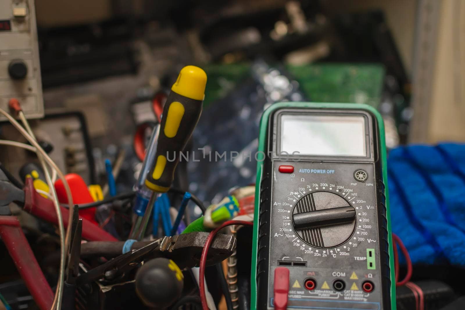 measurement scale on a multimeter, tester of electronic parts, components against the background of screwdrivers, tools, printed circuit boards, circuits and broken equipment in a repair service center