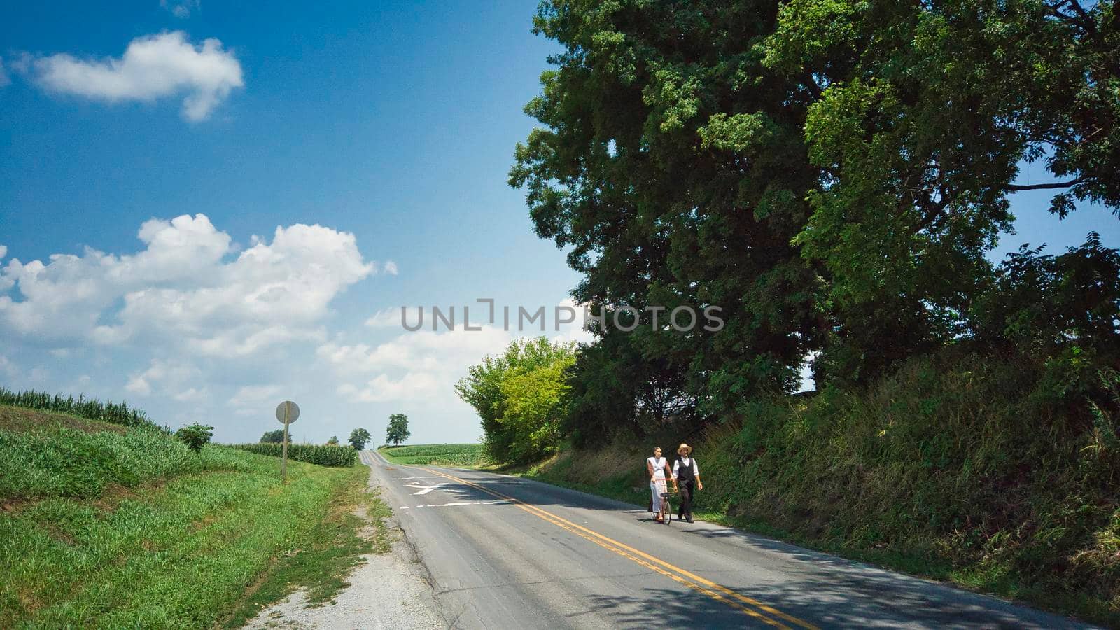 Ronks, Pennsylvania, July 2020 - An Amish Couple One Walking and One on a Scooter on a Road on a Summer Day