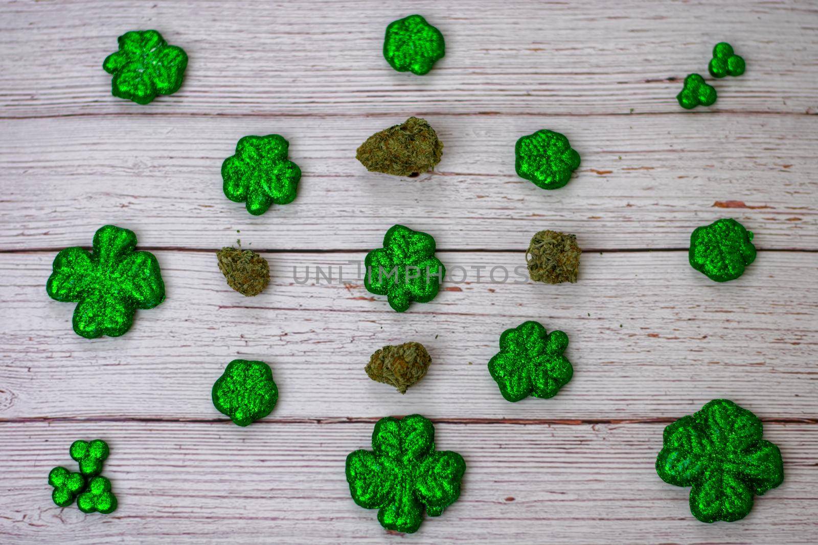 Glitter Covered Four Leaf Clovers and Cannabis Nugs in a Pattern on a White Wood Background by bju12290