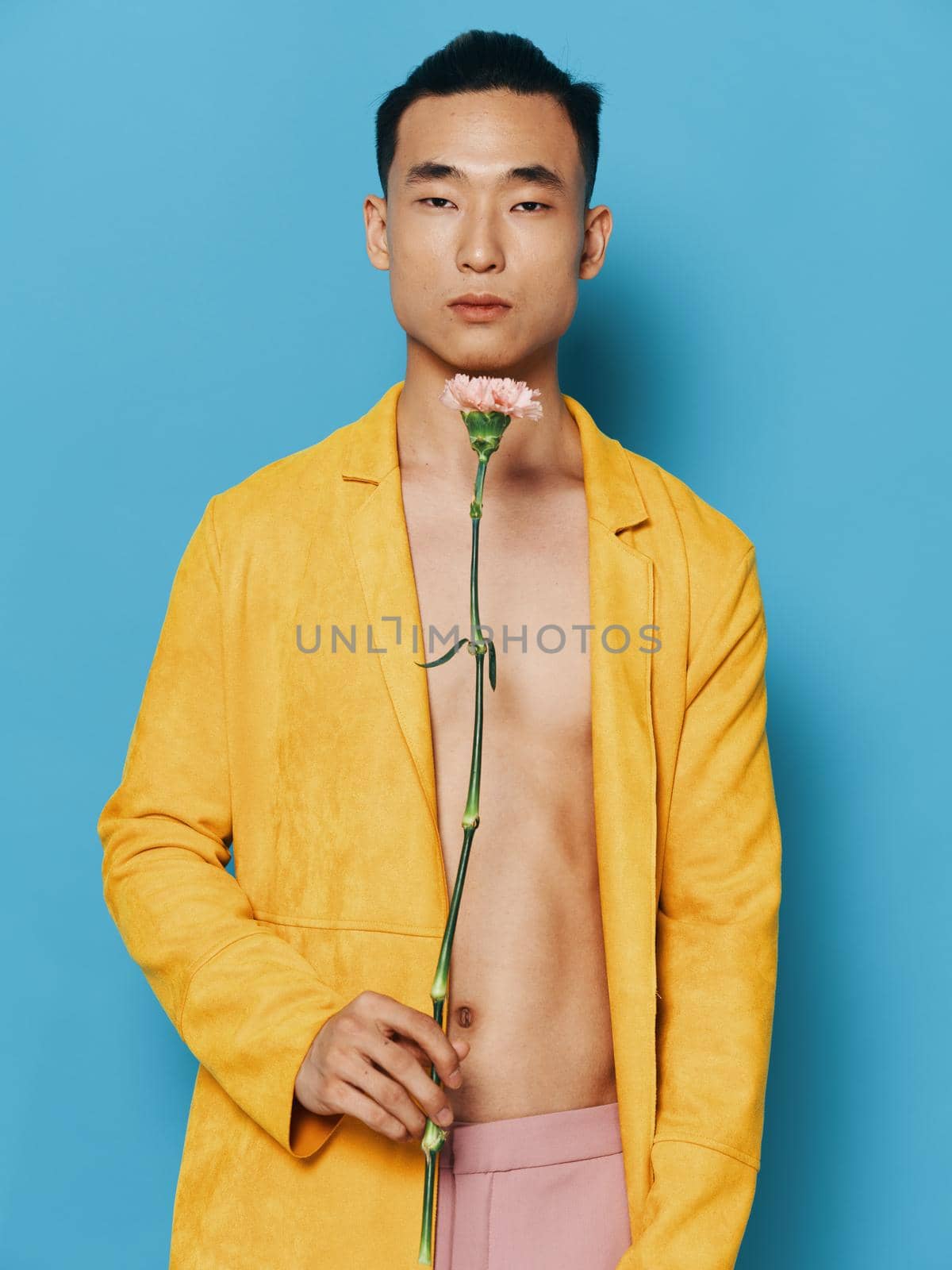 A guy with a beautiful flower in his hands on a blue background in a yellow coat. High quality photo