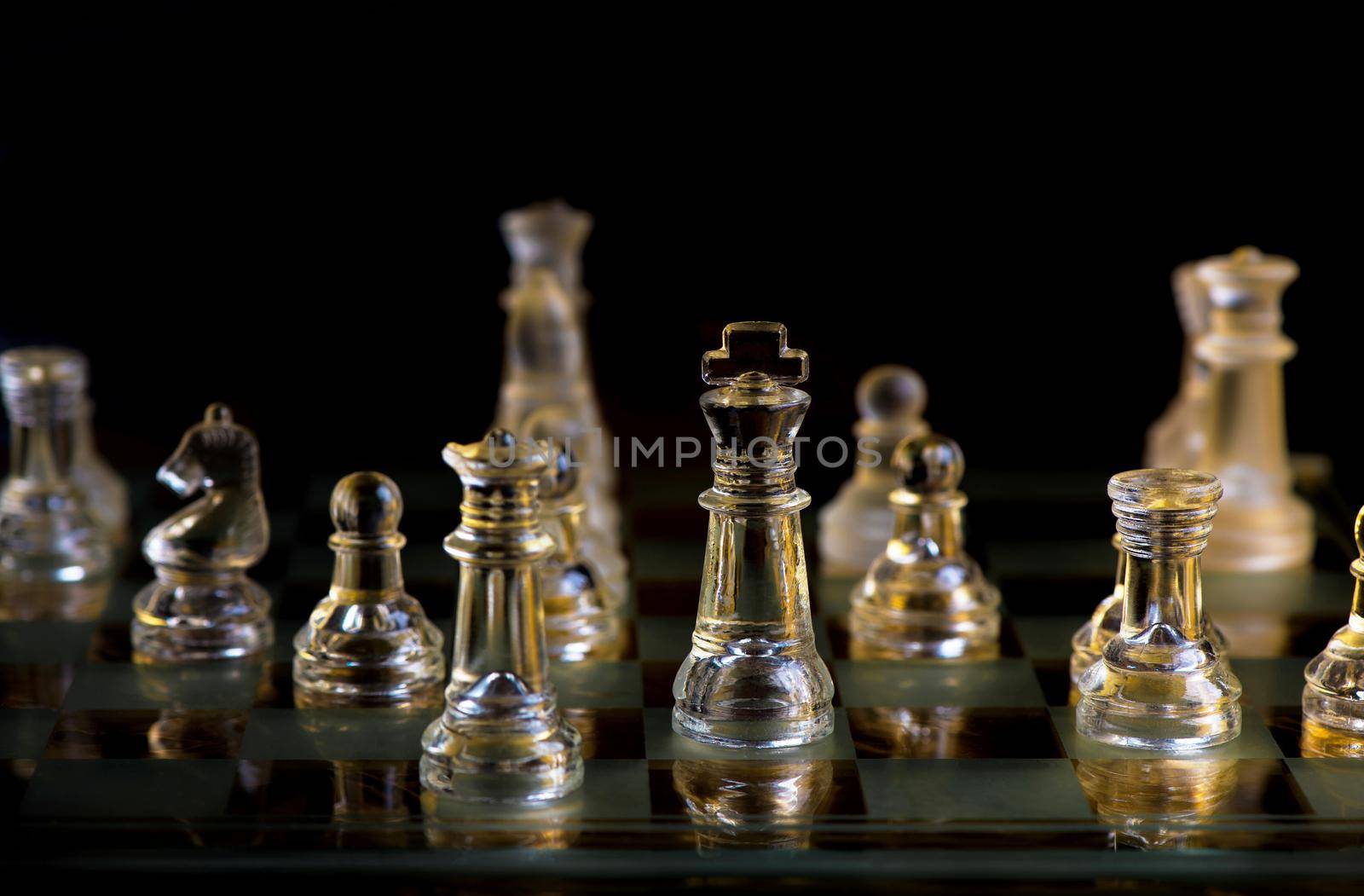 glass chess pieces are defending the king on board in dark by aprilphoto