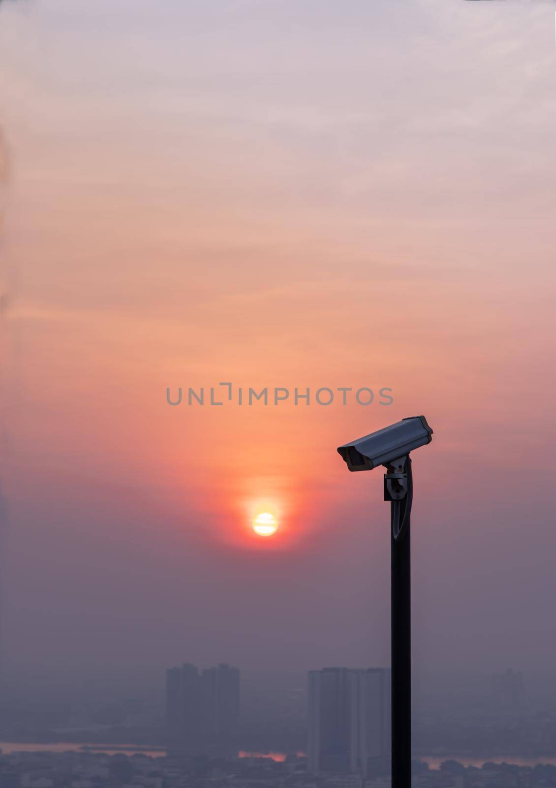 Modern surveillance camera on cityscape and skyscraper background with sun shing bright before the sun was setting. The concept of surveillance evening time, copy space, Selective focus.