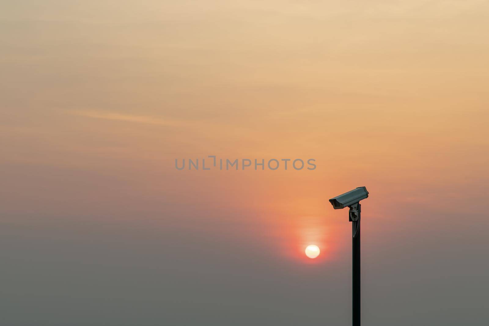 Modern surveillance camera in the foreground The orange sun shing bright before the sun was setting. The concept of surveillance evening time, copy space, Selective focus.