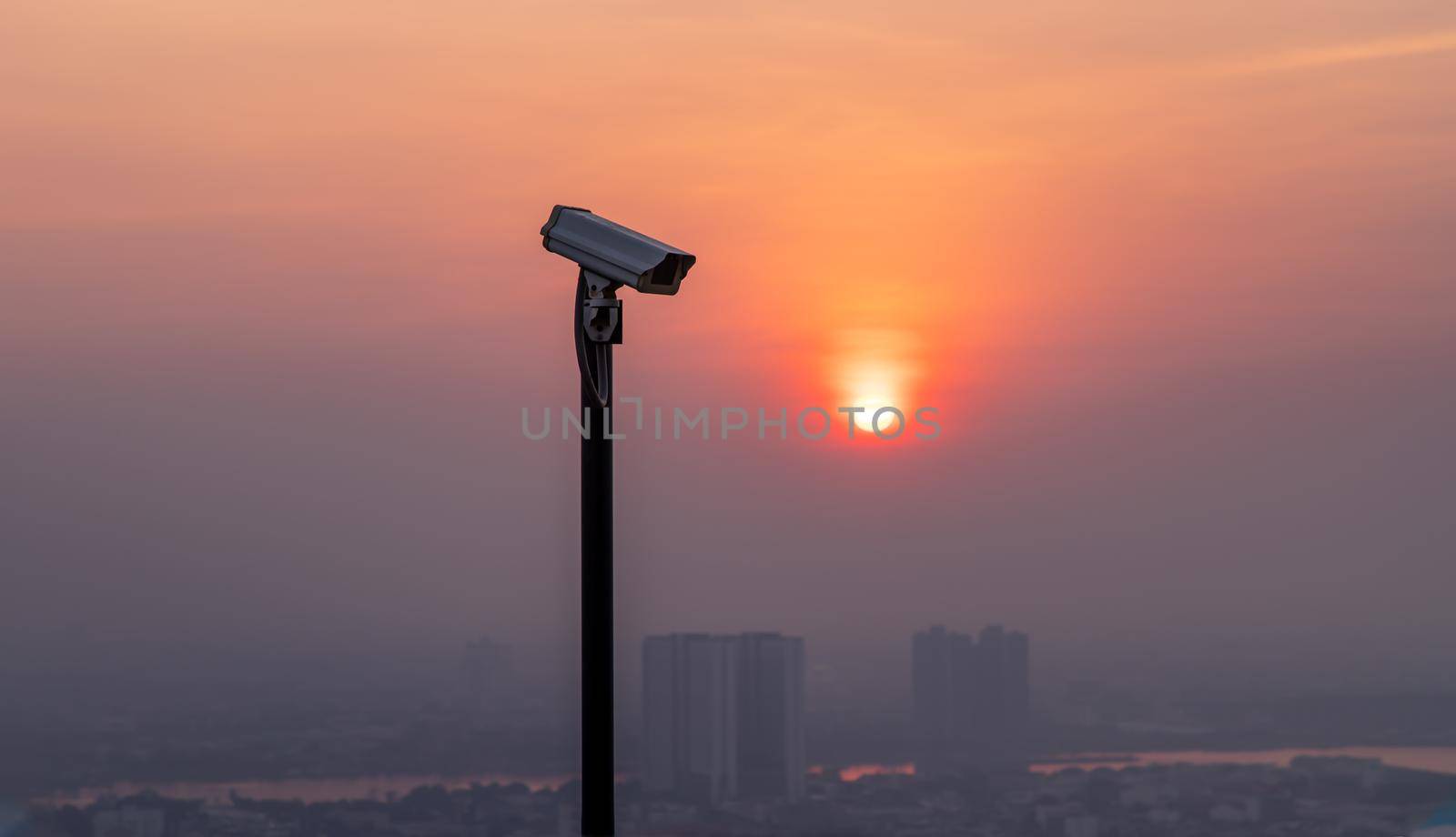 Modern surveillance camera on cityscape and skyscraper background with sun shing bright before the sun was setting. The concept of surveillance evening time, copy space, Selective focus.