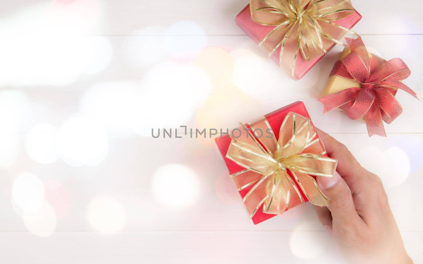 Hand holding gift box giving on wooden table in Valentine day or holiday bokeh background, presents for anniversary or birthday or celebration with copy space, celebrate and festive, top view.