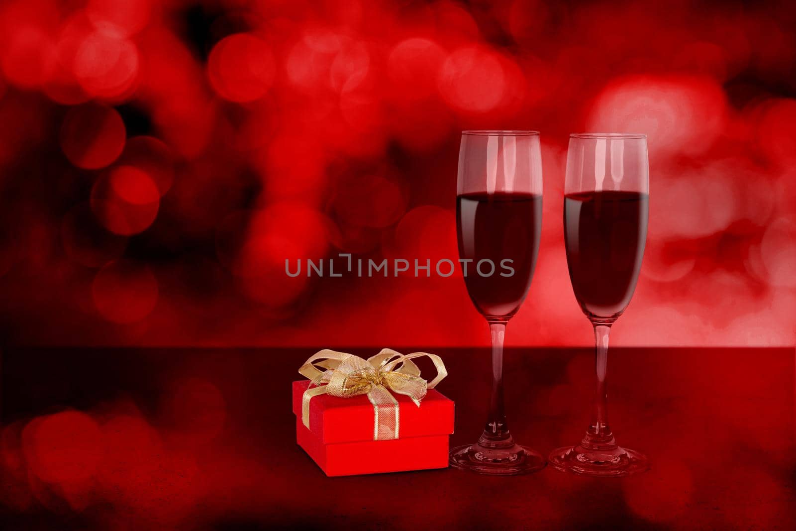 Two wineglasses and red gift box on desk with red blur bokeh background, champagne glasses and presents with celebration and anniversary, love and romantic, valentine day concept.