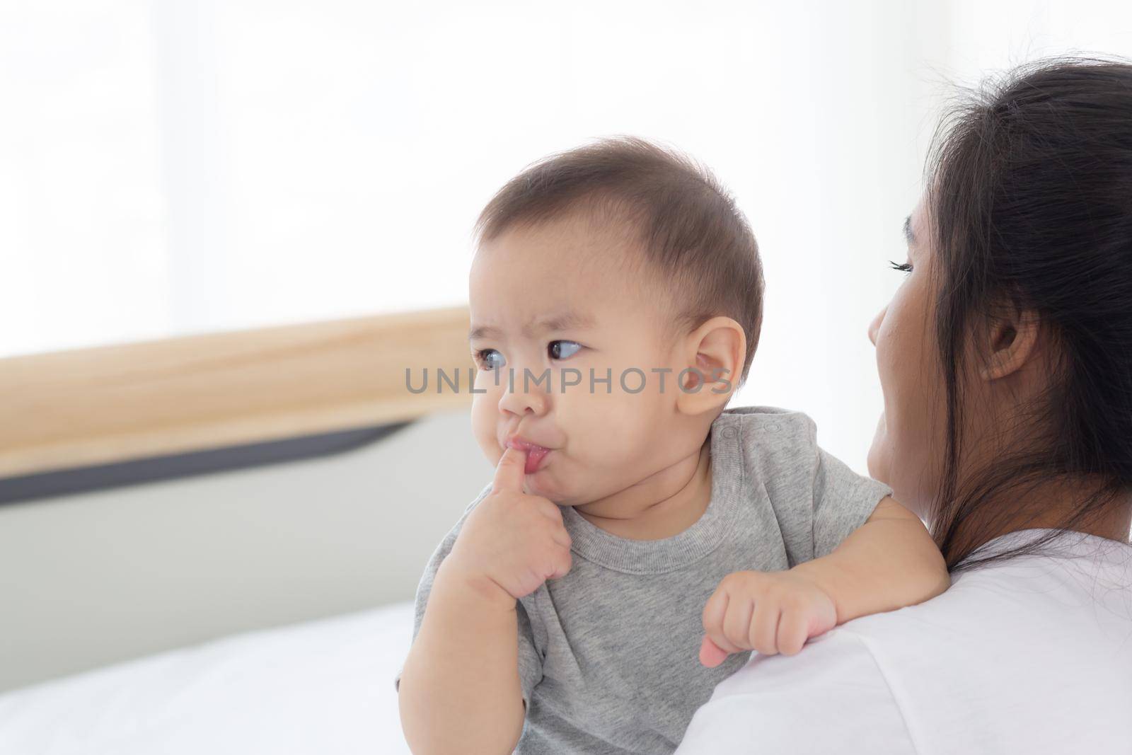 Young asian mother holding little baby girl together in the bedroom at home, mom carry child and care, woman and kid with carefree, toddler and parent, emotion and expression, family concept.