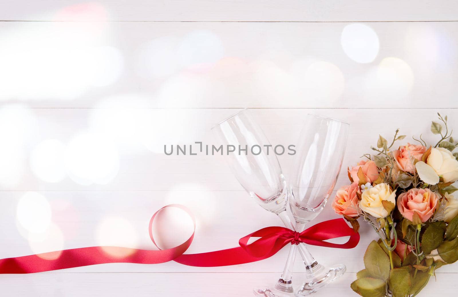Valentine day concept, wineglass and red ribbon and flower on white wooden table background with bokeh, champaign glass on wood desk, top view, couples wine glass together, romantic holiday concept. by nnudoo