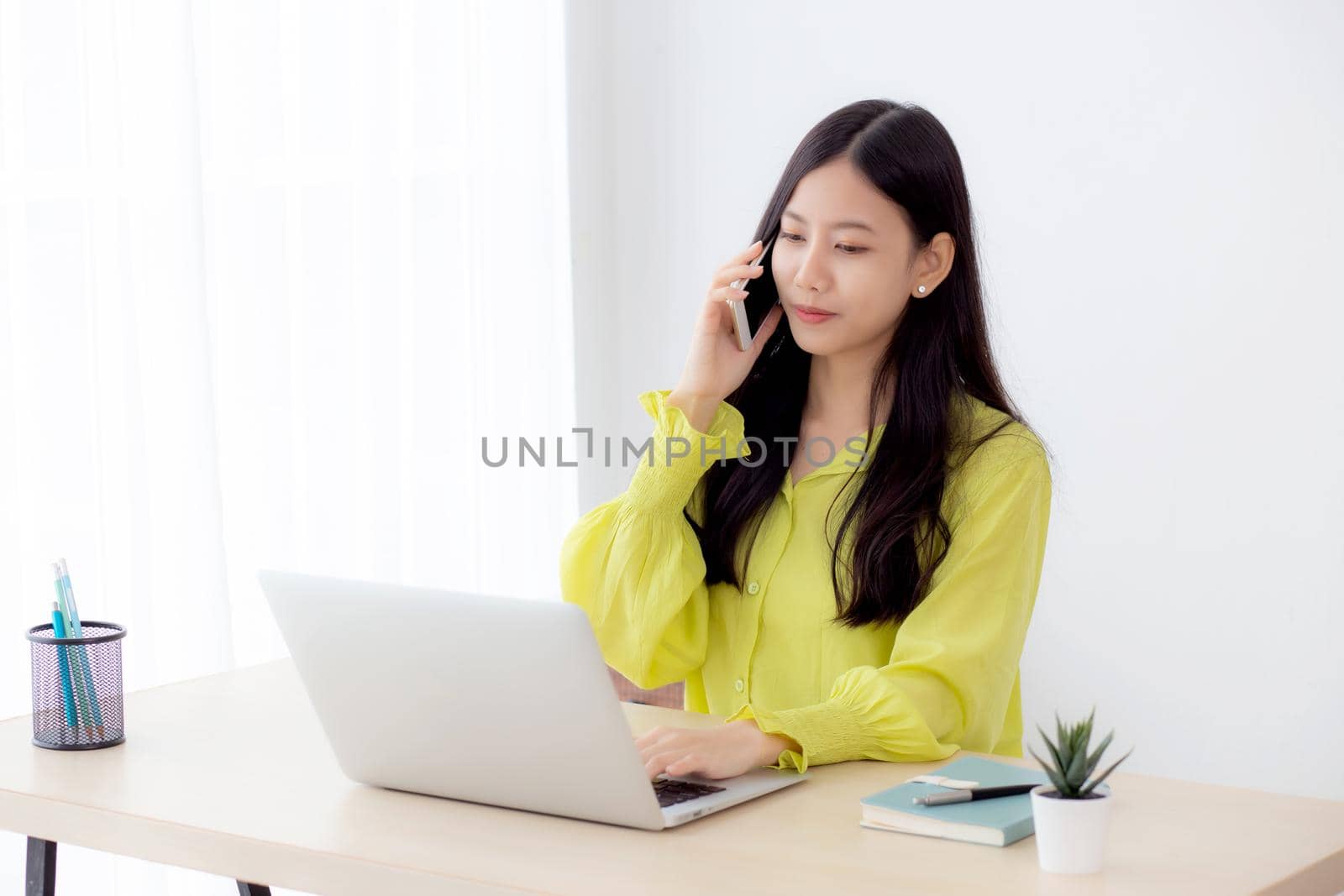 Young asian business woman working form home office and call phone for success at home, businesswoman using laptop computer on desk, female talking smartphone at workplace, communication concept.