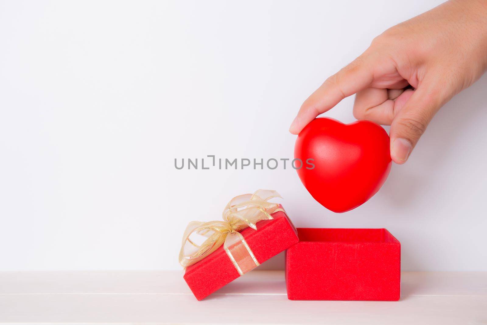 Valentine day, hand open red gift box put heart, celebration and anniversary with giving love, donate and aid with heart shape symbol, charity and health, copy space, holiday and festive concept.