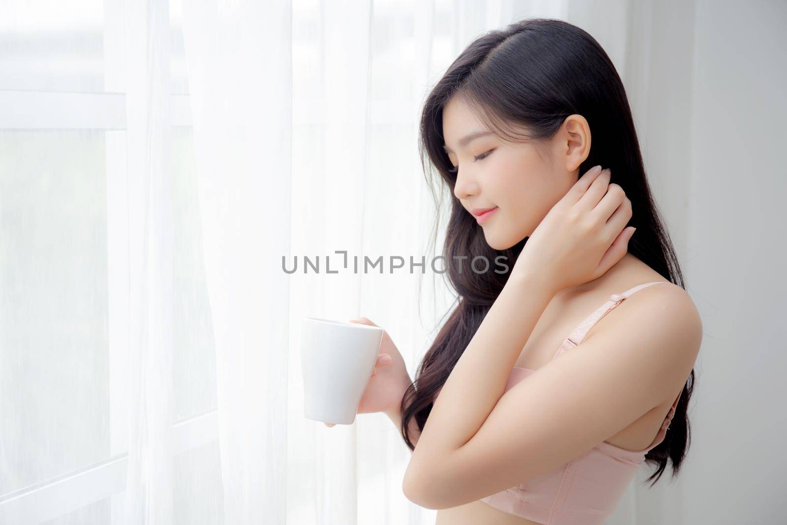 Beautiful young asian sexy woman in underwear drinking coffee near windows in the morning, girl with seductive figure fit drinking beverage for relax and resting after wake up, lifestyle concept.