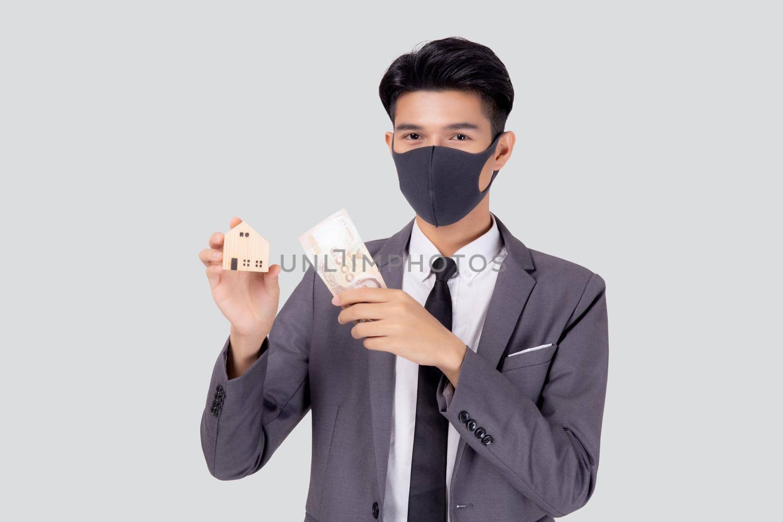 Young asian businessman in face mask holding money Thai and home isolated on white background, pandemic and crisis of economic, business man and investment property during disease covid-19.