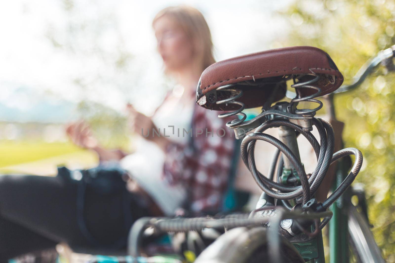 Closeup picture of brown vintage bicycle seat, blonde girl sitting in blurry background