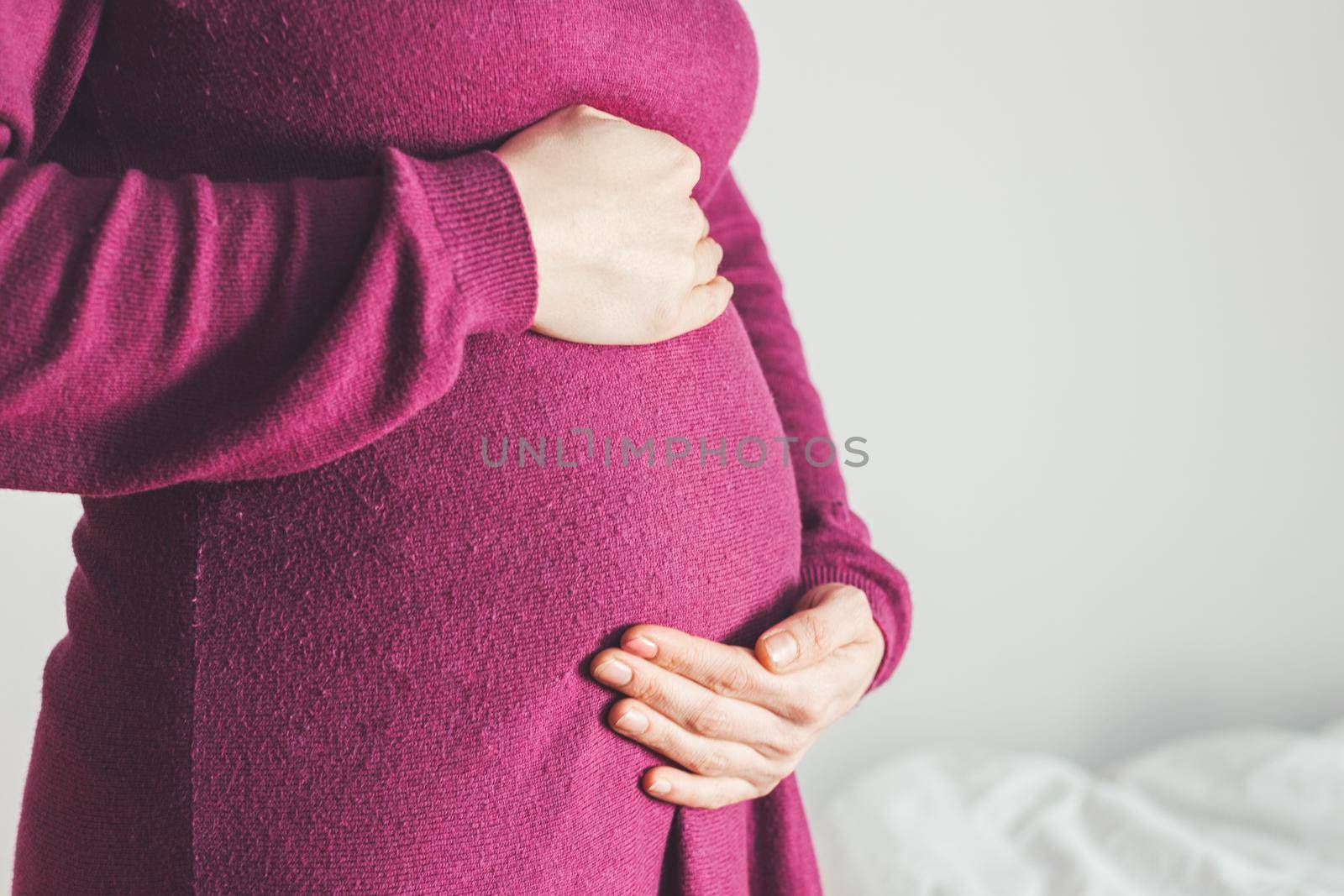 Close up of pregnant tummy, Caucasian mother in magenta dress