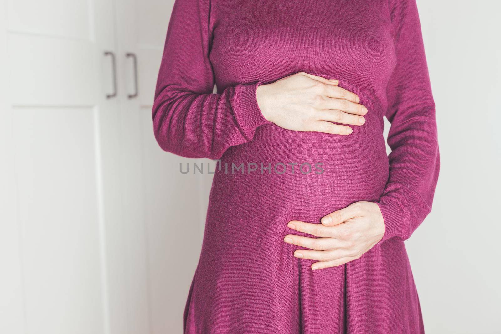 Close up of pregnant tummy, Caucasian mother in magenta dress
