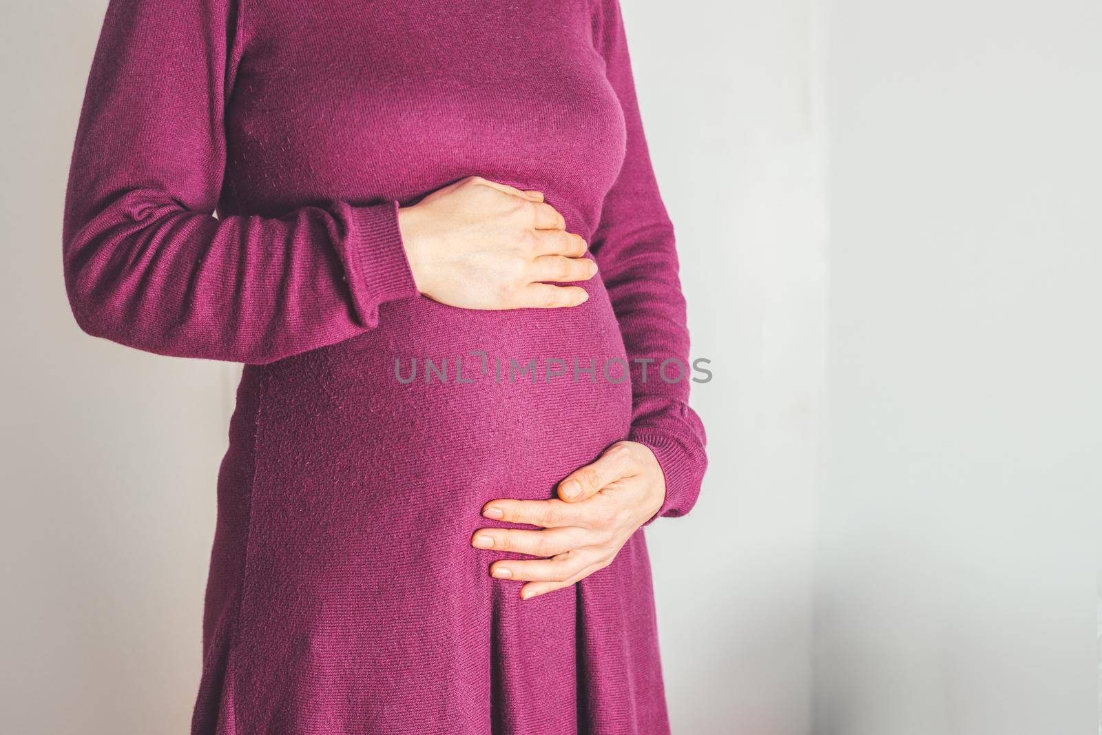 Close up of pregnant tummy, Caucasian mother in magenta dress