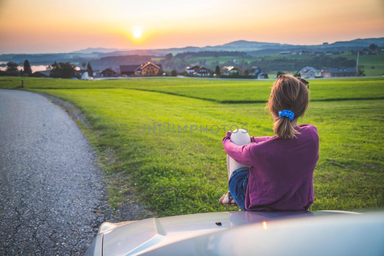 Young woman sitting on a car, enjoying the sunset