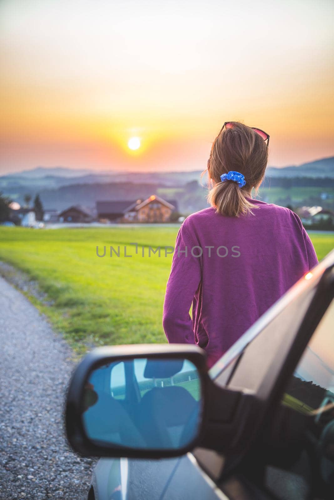 Young woman sitting on a car, enjoying the sunset
