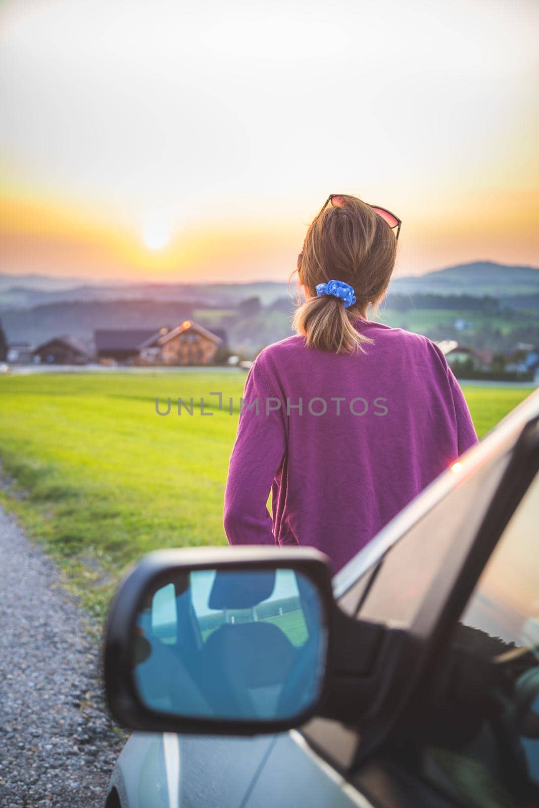 Young woman sitting on a car, enjoying the sunset