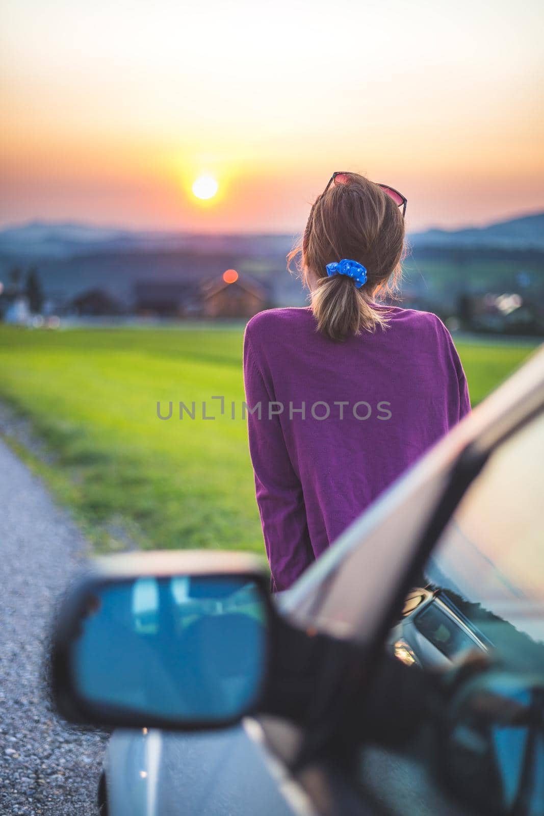 Young woman sitting on a car, enjoying the sunset