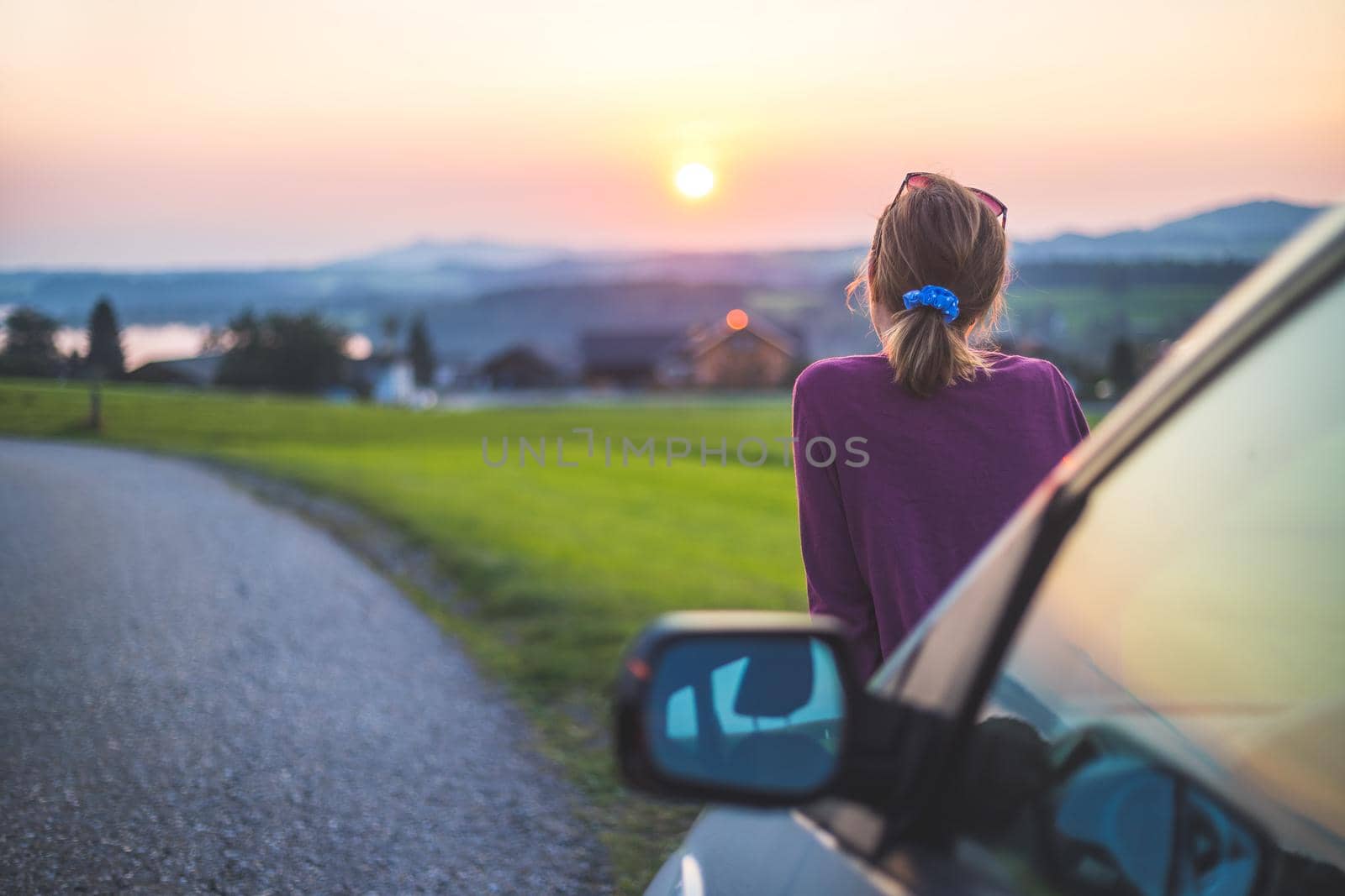 Young woman sitting on a car, enjoying the sunset