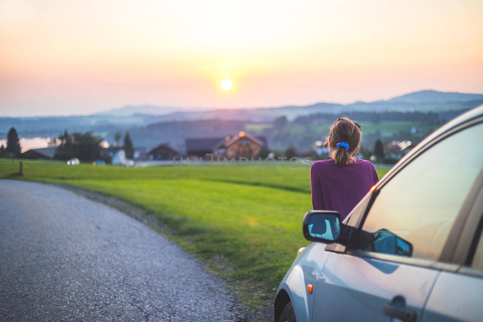 Young woman sitting on a car, enjoying the sunset