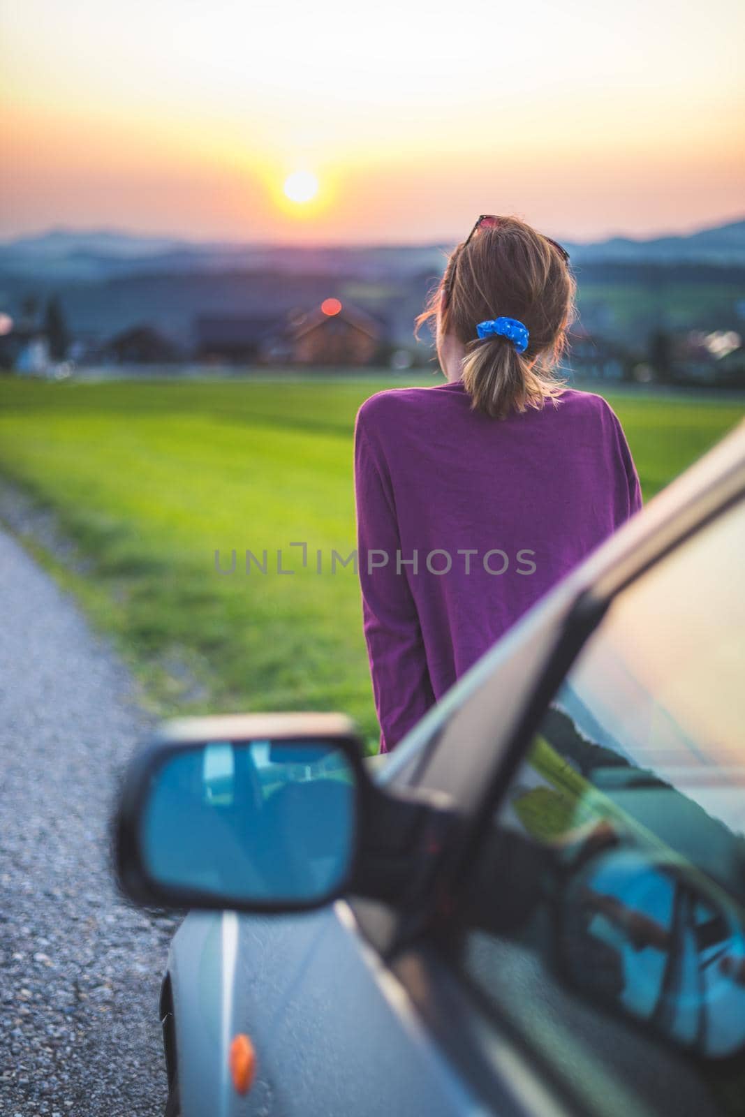 Young woman sitting on a car, enjoying the sunset