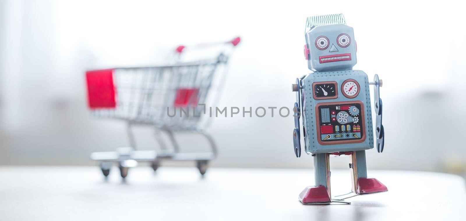 Online shopping algorithm concept. Toy robot on the desk, shopping cart in the blurry background by Daxenbichler