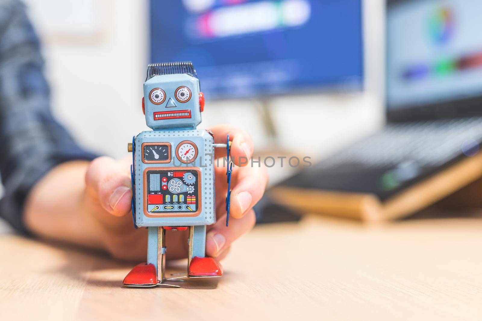 Toy robot on a desktop, man working on the computer in the background. Symbol for artificial intelligence, chatbots or social bots and algorithms