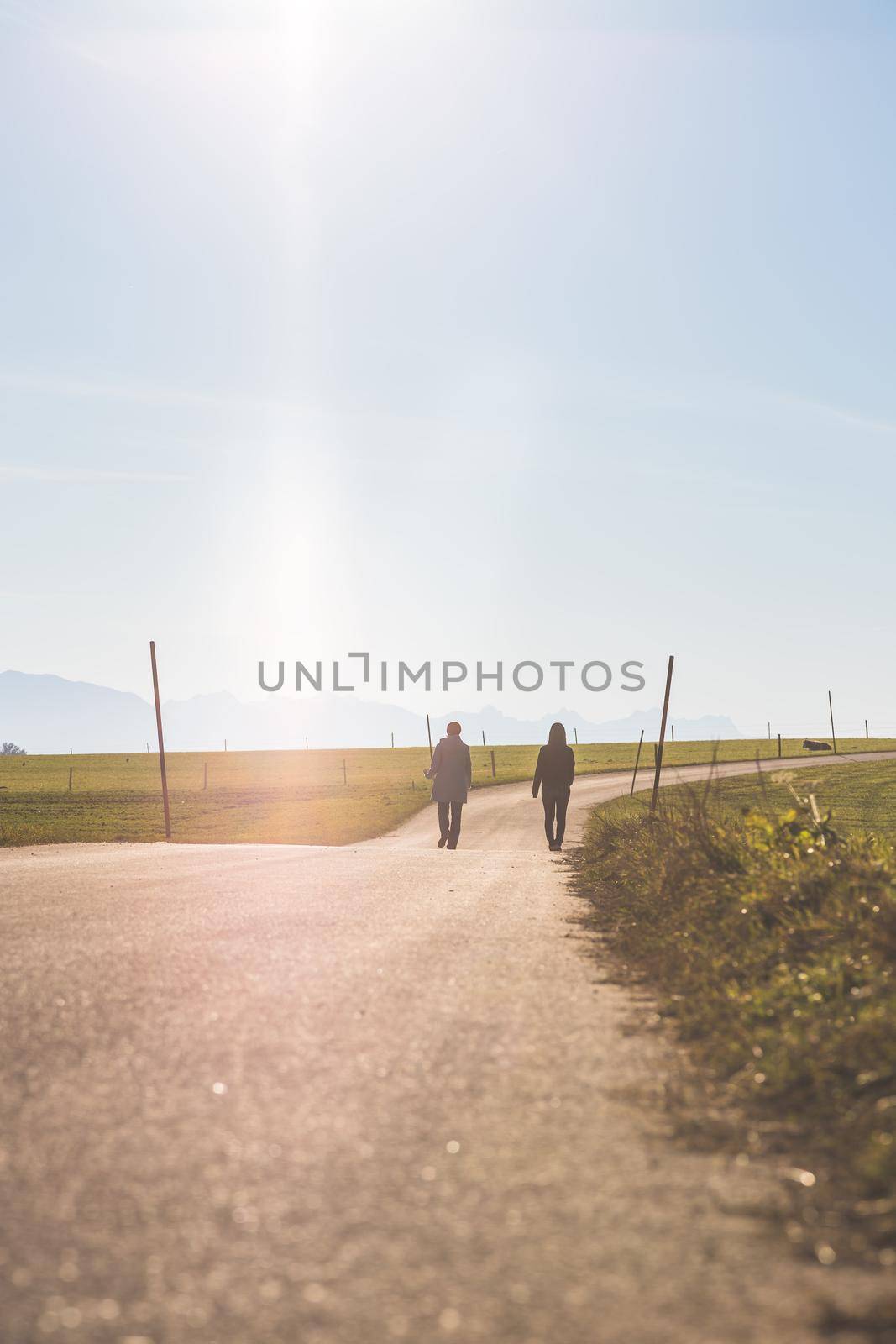 Two people are walking on asphalted road by Daxenbichler