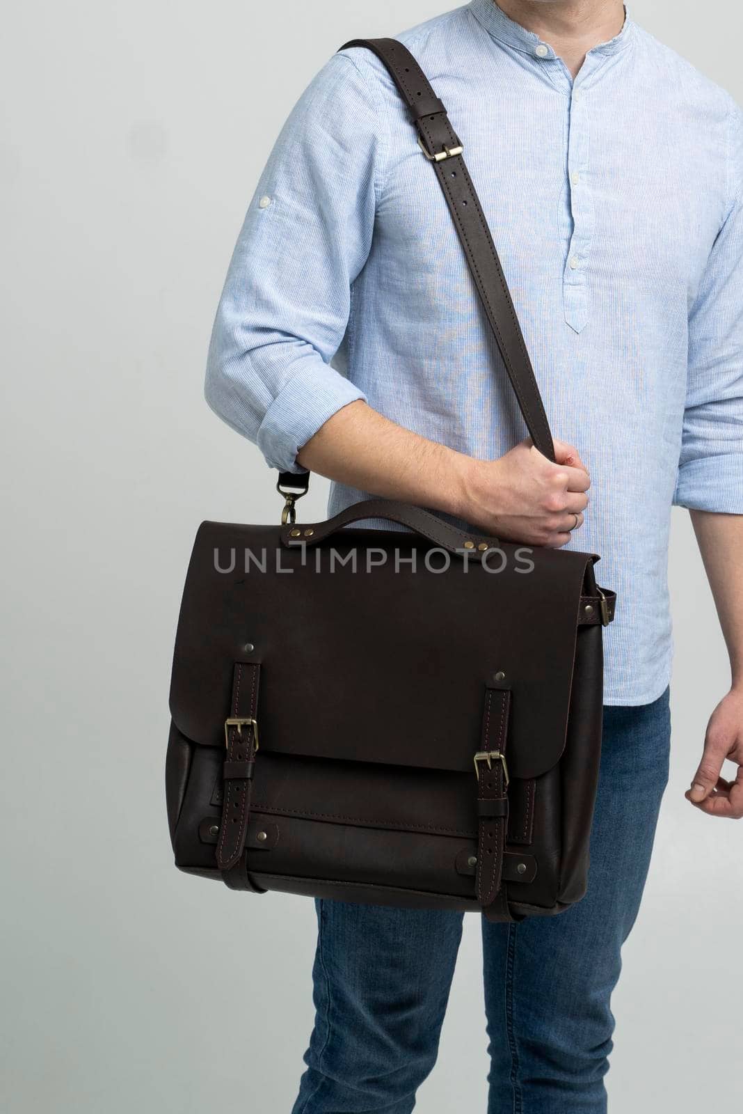 Brown men's shoulder leather bag for a documents and laptop on the shoulders of a man in a blue shirt and jeans with a white background. Satchel, mens leather handmade briefcase. by vovsht