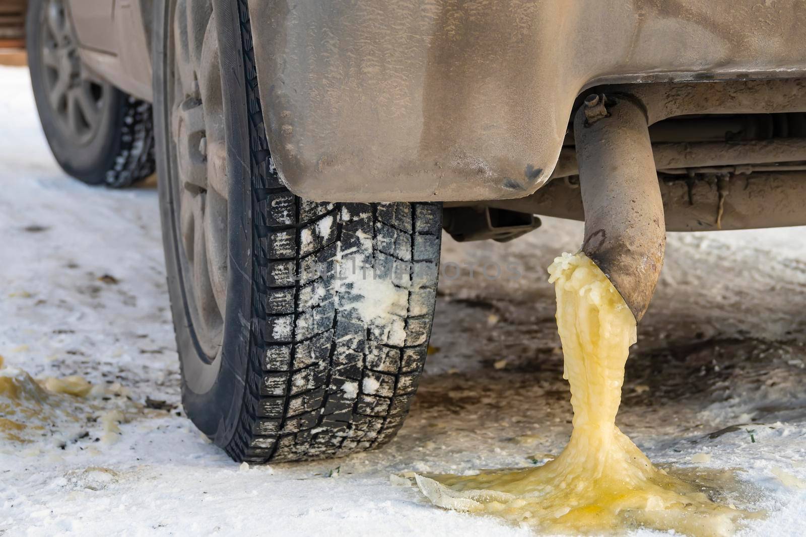 frozen yellow water condensate with gasoline from the exhaust pipe of a car on the snow in the cold winter season