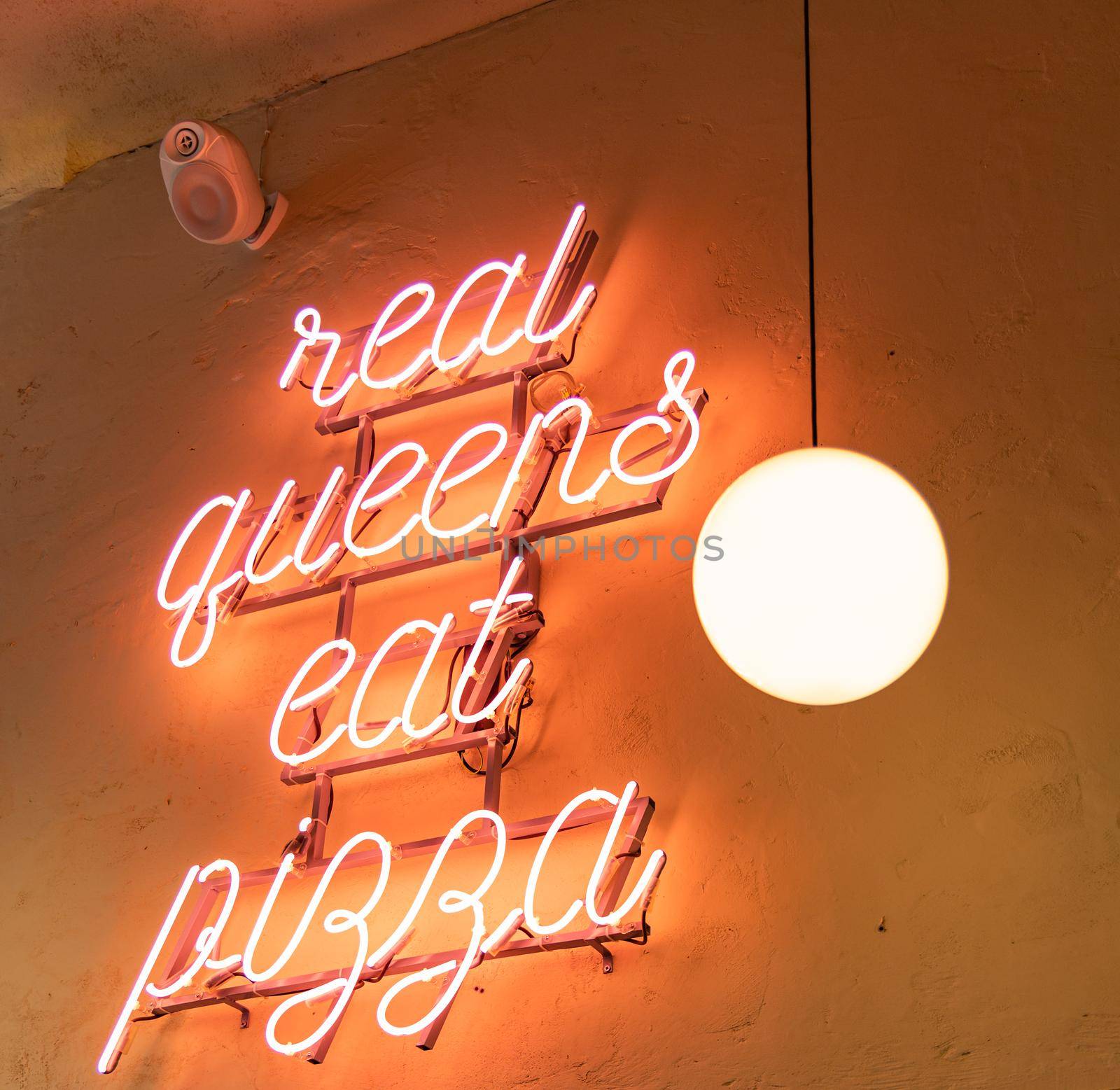 Glowing light neon "real queens eat pizza" hanged on wall near sphere lamp by Wierzchu