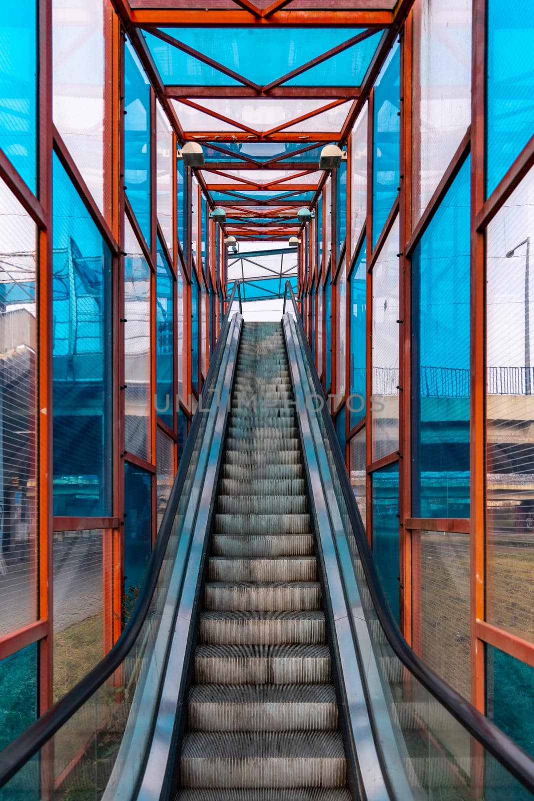 Long escalator to bridge over street with colorful windows around by Wierzchu