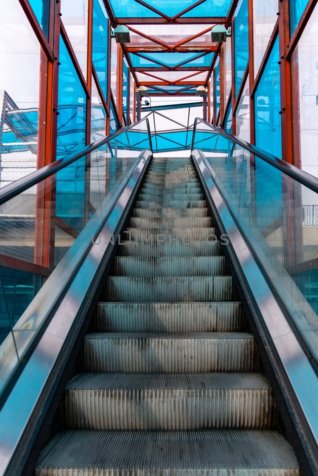 Long escalator to bridge over street with colorful windows around